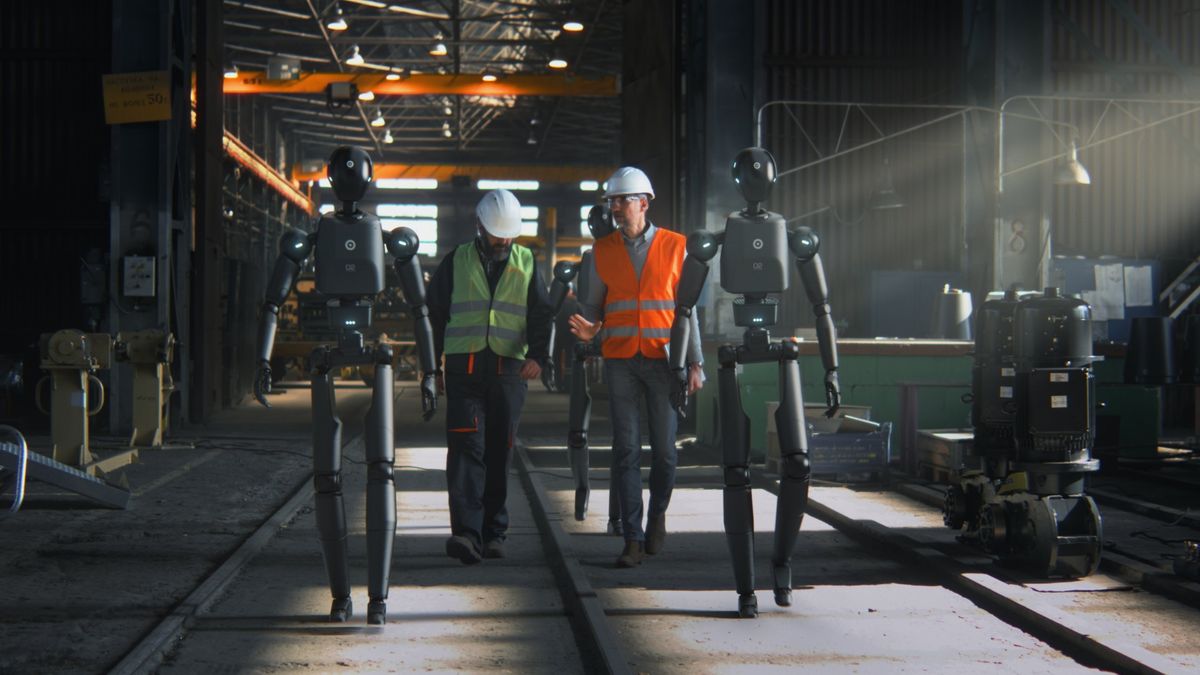Engineers walking through a workshop alongside humanoid robots